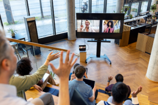 Audience engagement tool in action as a group waves to two individuals on a large screen during a video conference call.