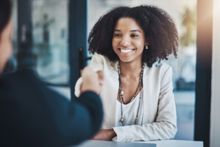 A smiling woman in a business setting shakes hands, symbolizing successful planning and collaboration.