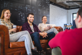 Three young professionals smiling and conversing on a leather couch in a modern office, showcasing event storytelling.